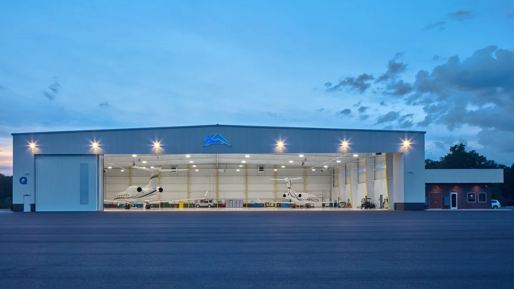 Illuminated aircraft hangar at dusk with private jets inside a steel-framed facility